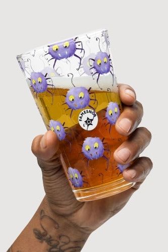 Hand holding a glass with a purple cartoon character design and a visible brand logo.